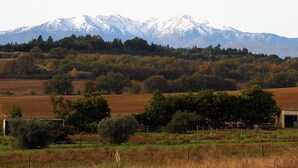 A mountainous landscape with a field in the foreground and a building in the distance. - Asinerie Kuleni (Ponteilla)
