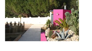 A pathway leading to a building with a pink exterior, surrounded by cacti and a wooden fence. - Asinerie Kuleni (Ponteilla)
