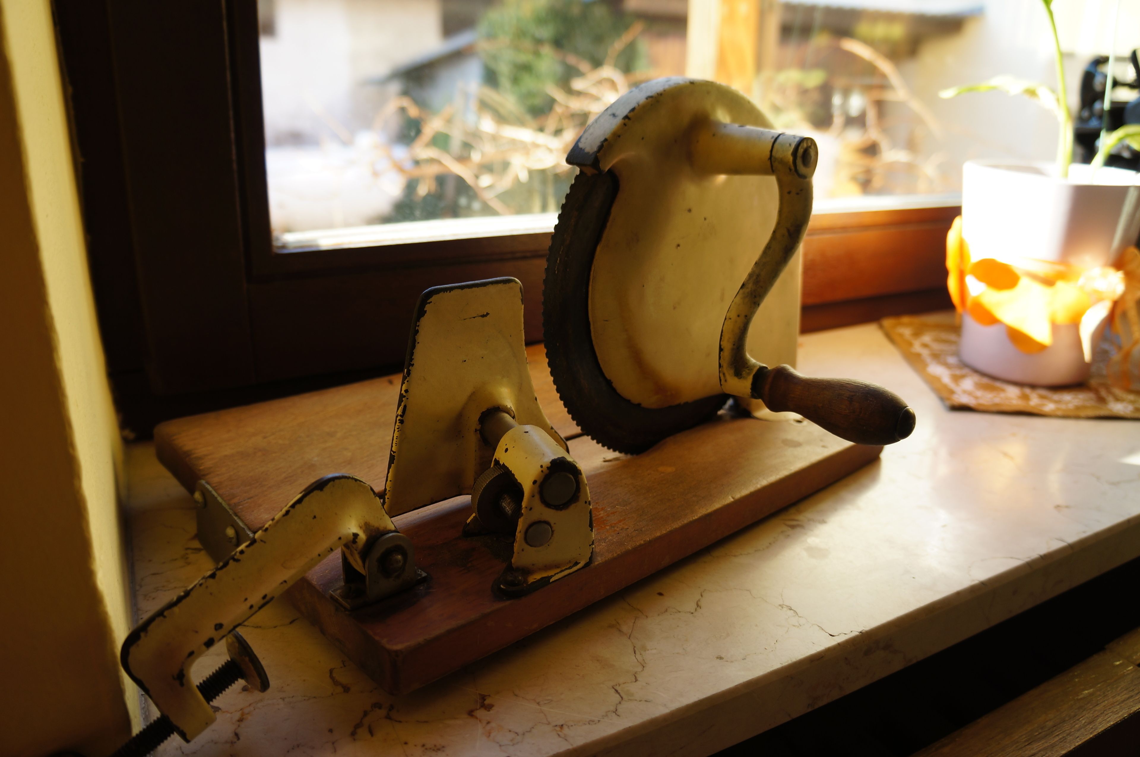 A rustic kitchen with a wooden countertop, a vintage meat slicer, and a window with a view of dried plants.