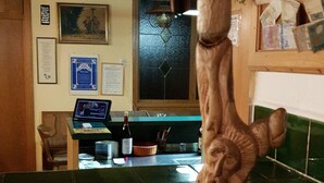 A bar area with a wooden sculpture, a laptop on a counter, and various framed items on the wall. - Gasthof Bauer (Elsendorf)