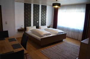 Quarto com cama de madeira, mesa de jantar com cadeiras, parede estampada e janela com cortinas.
