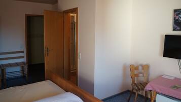Habitación de hotel con cama, una silla de madera, un escritorio con mantel rosa, televisor y armario.