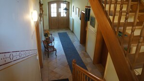 A staircase leading to a landing with a wooden handrail, a blue carpet, and a door with a window. - Gasthof Bauer (Elsendorf)