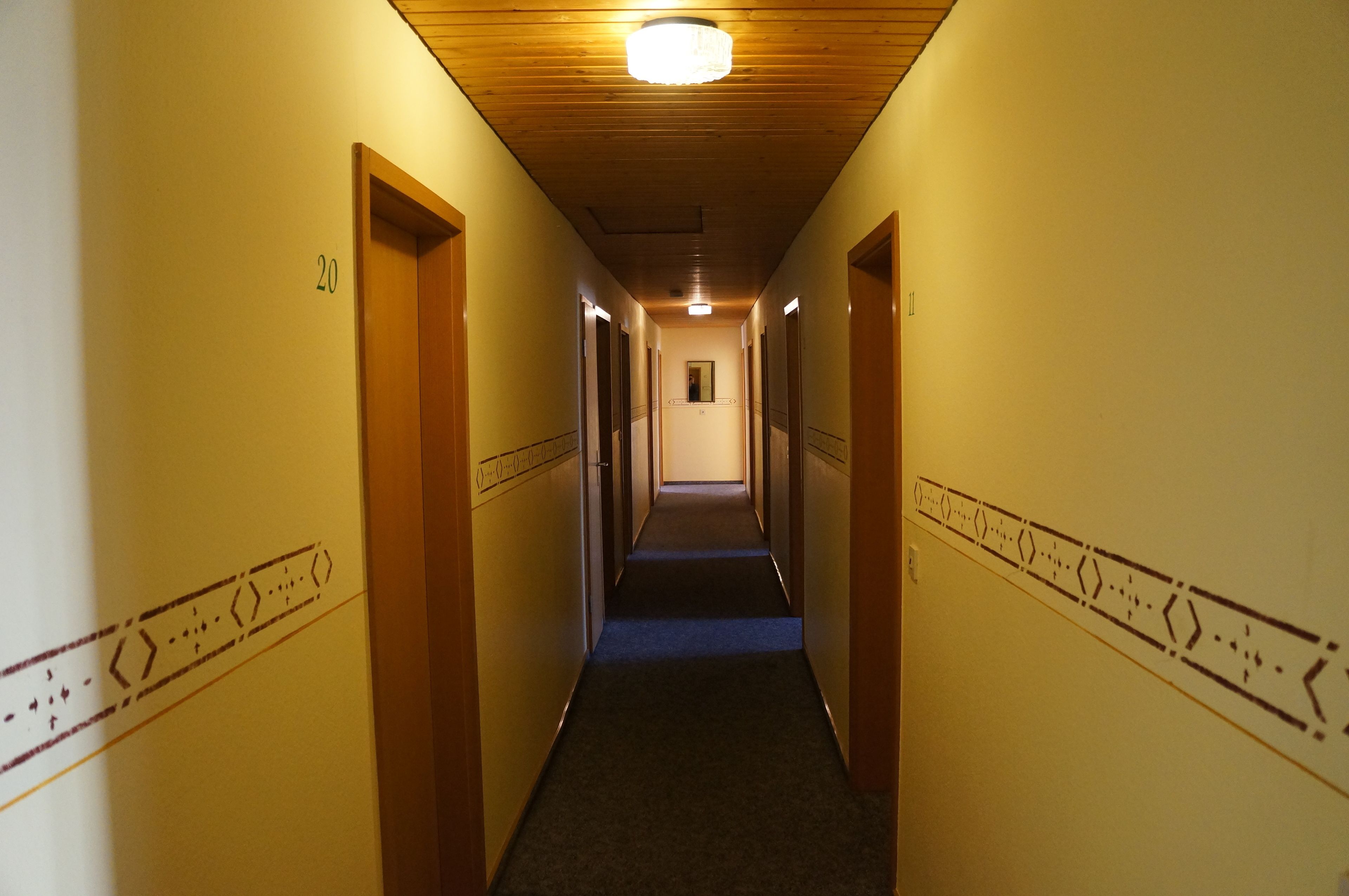 En hall med dörrar av trä, numrerade från 20, och ett golv täckt av matta.