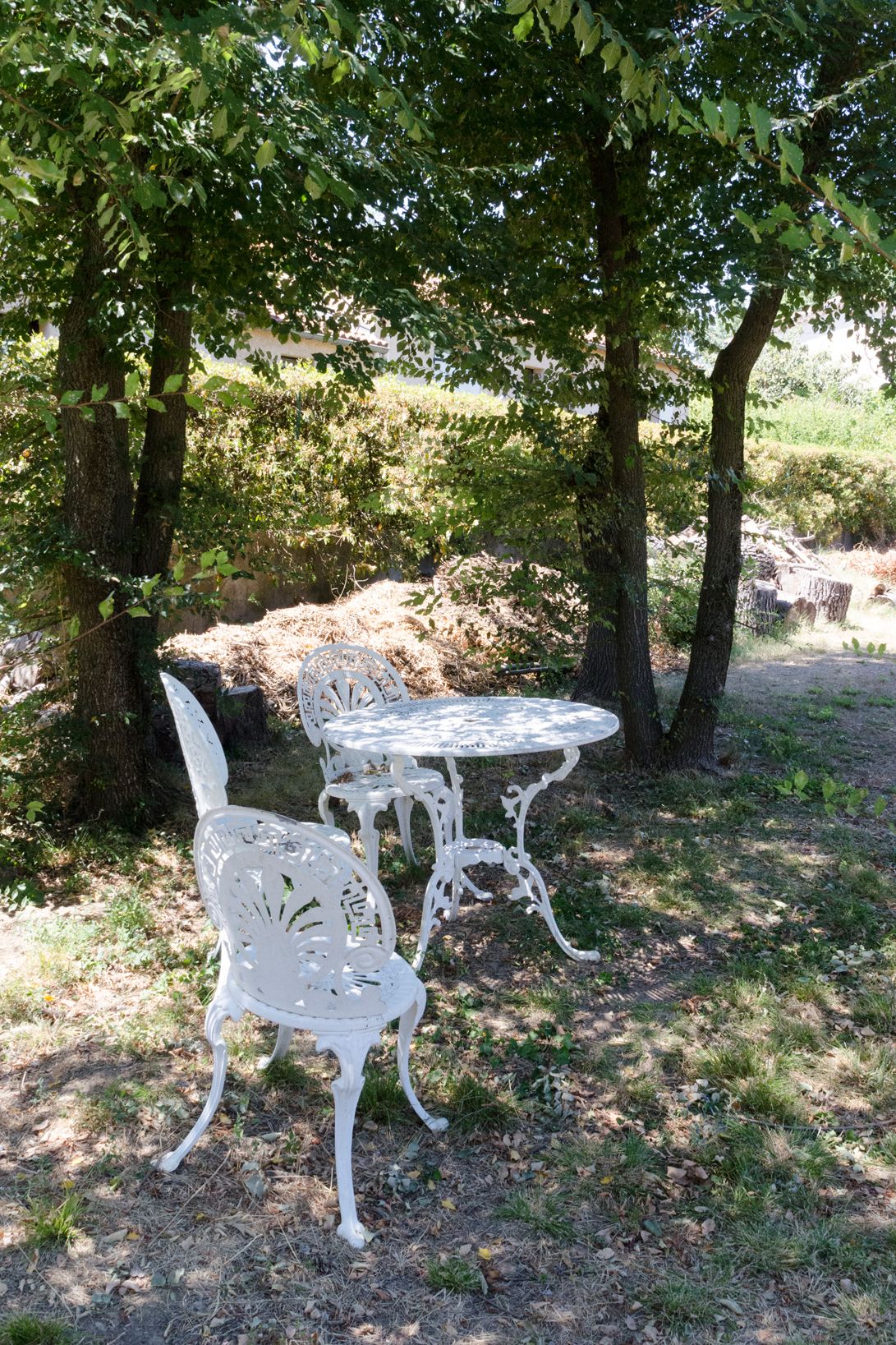 Un ensemble de table et de chaises en métal blanc, placé à l’extérieur, sous un arbre, dans un cadre naturel.