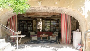 An outdoor reading area with a sofa, a table, and a bookshelf under an arched stone structure. - MAS ABICOU - chambres d'hôtes (Vezenobres)