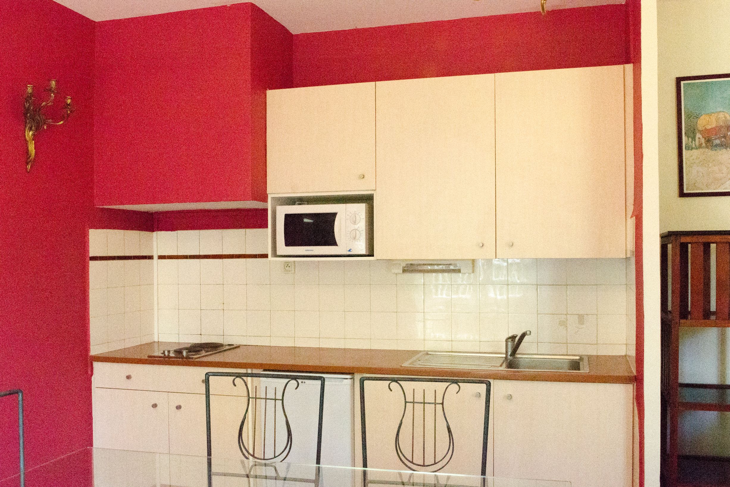 A compact kitchen with white cabinets, a microwave, and a sink. There are two chairs with a unique design.