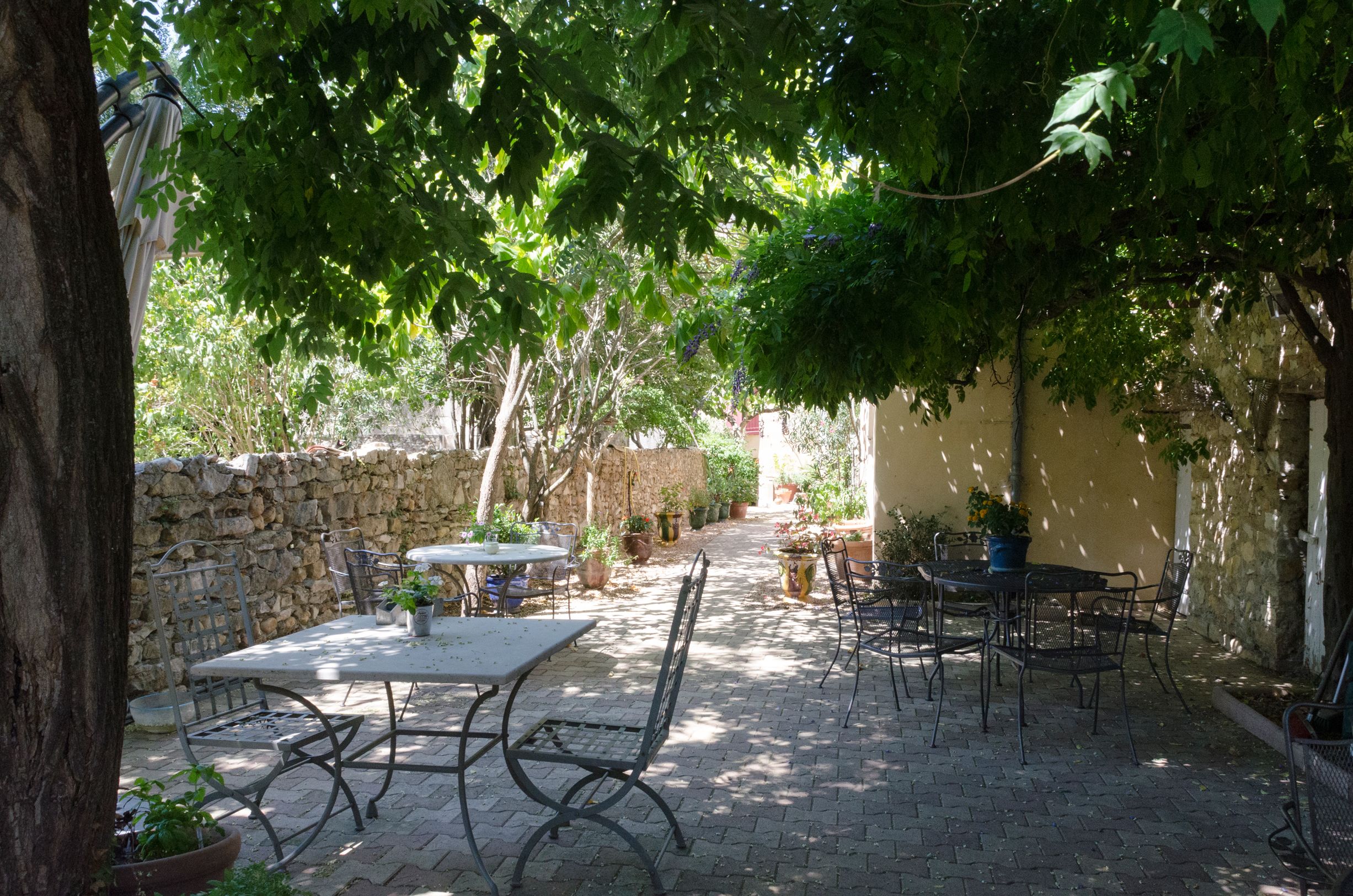 An outdoor patio area with stone walls, potted plants, and metal tables and chairs.