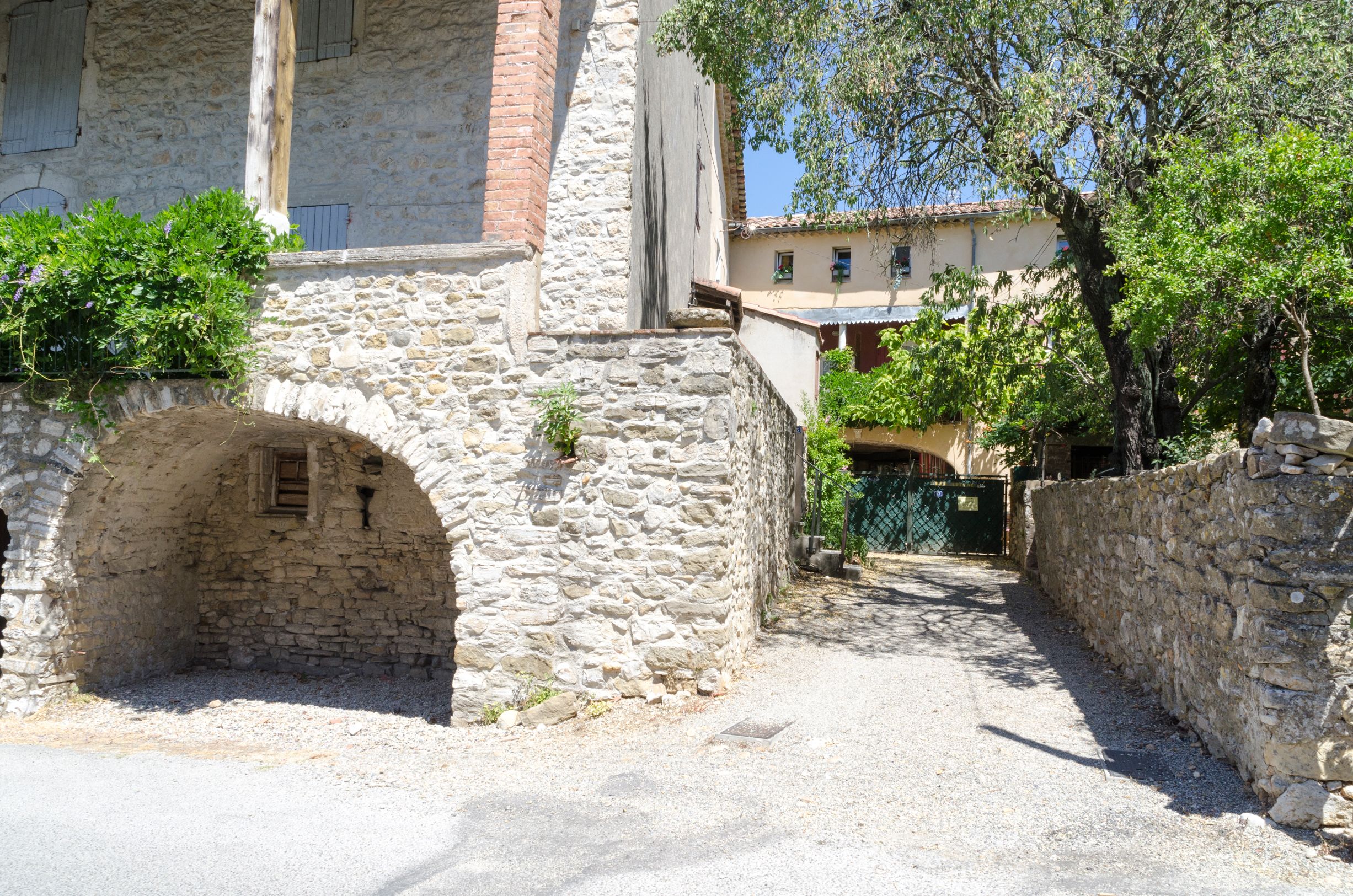 A narrow stone pathway leading to a rustic building with a stone archway and a small window.