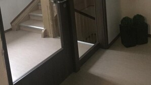 A hallway with a glass door leading to a staircase, a fire extinguisher mounted on the wall, and two potted plants.