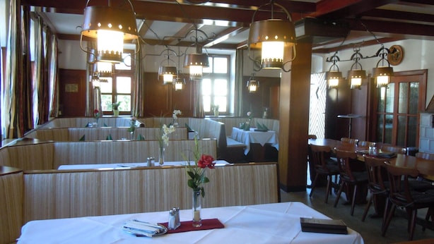 A restaurant with booths and a long table, both with white tablecloths. There are hanging lights above the booths and table.