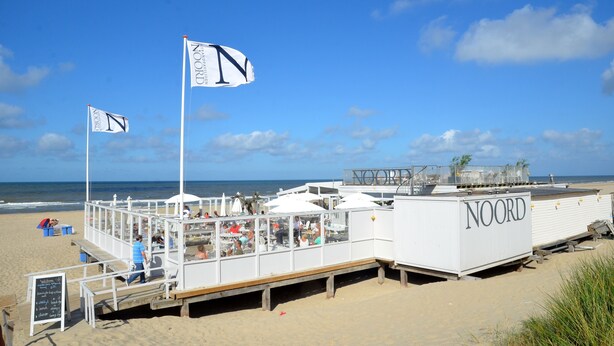 A beachside restaurant with outdoor seating, a deck, and a sign reading "NOORD". - Beach House Sea-Side (Egmond aan Zee)