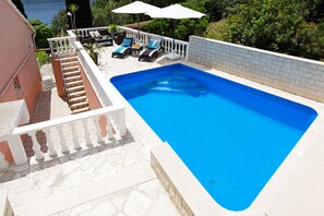 A rectangular swimming pool with a white tiled deck, a white balustrade, and a set of lounge chairs with blue cushions. - House Ivan (Vela Luka)