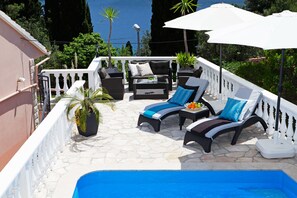Ein sonniger Sitzbereich im Freien mit Pool, weißen Geländern und Topfpflanzen.
