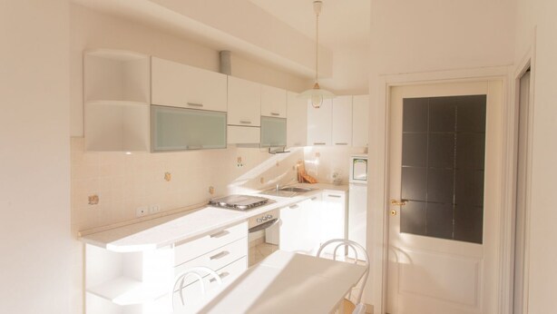 A modern kitchen with white cabinetry, a built-in oven, and a dining area with a white table and chairs. - N044 - Numana, new three-room apartment with terrace and a / c (Numana)