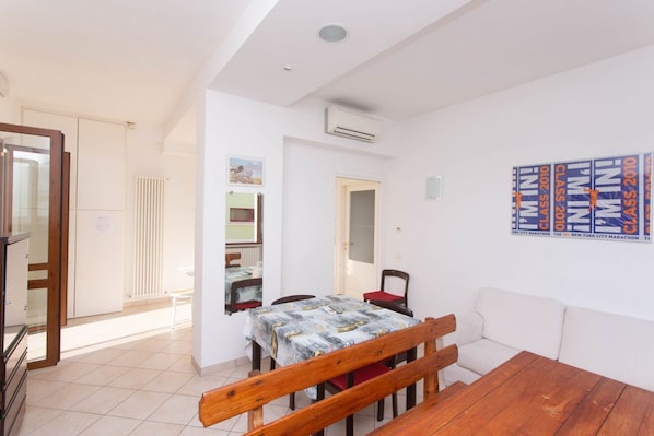 A room with a wooden table, a bench, a dining table with chairs, a white sofa, and a wall with marathon posters.