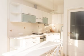 A modern kitchen with white cabinets, a built-in oven, and a dining area with a white table and chairs.