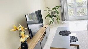 Une chambre moderne dotée d’un téléviseur à écran plat, d’une table en bois, d’une plante en pot et d’une grande fenêtre avec des rideaux.