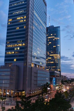 A high-rise building with multiple floors and a glass facade, surrounded by other buildings and a busy street with vehicles.