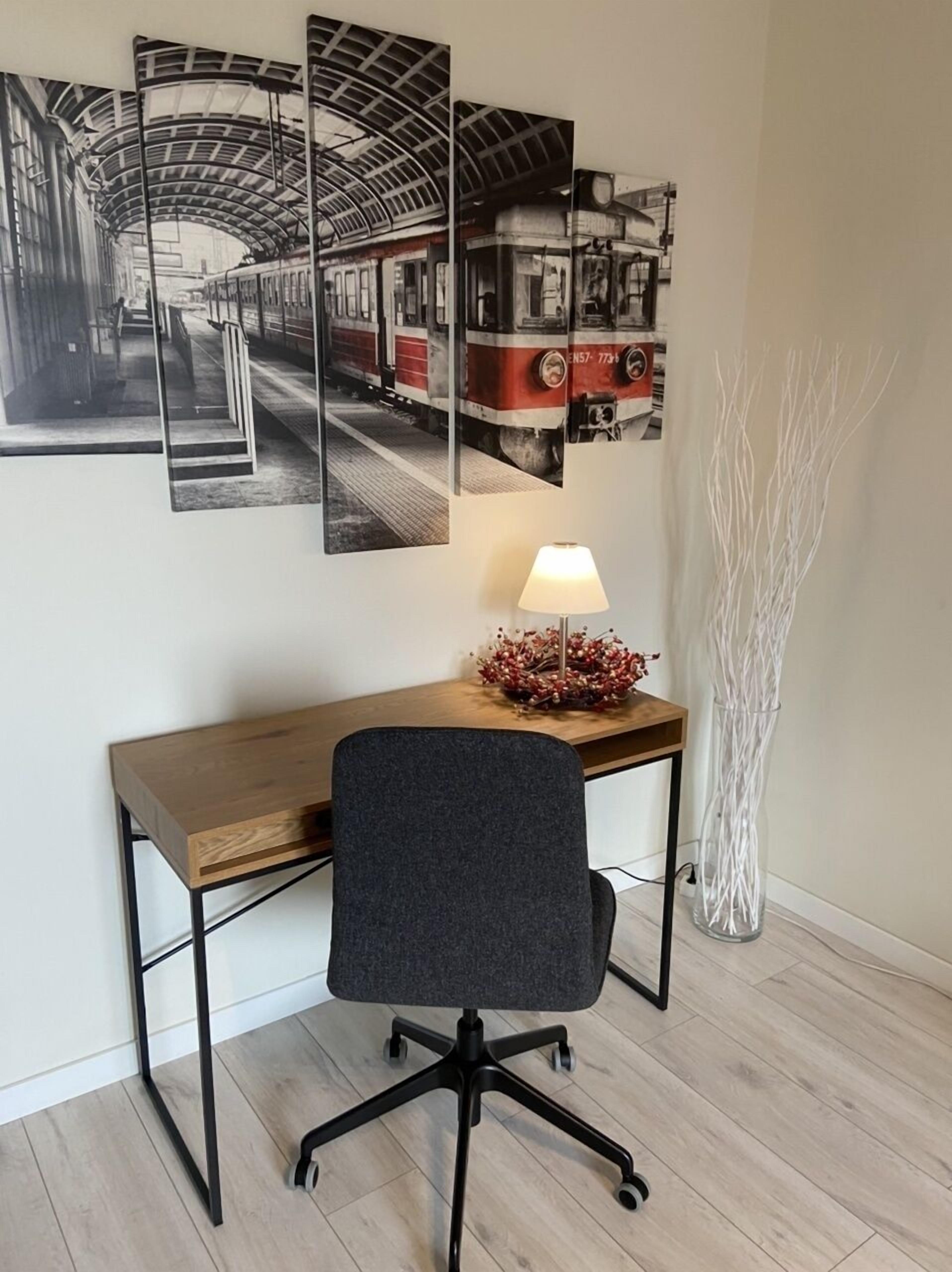 A modern office space with a wooden desk, a black office chair, a standing lamp, and a decorative vase.