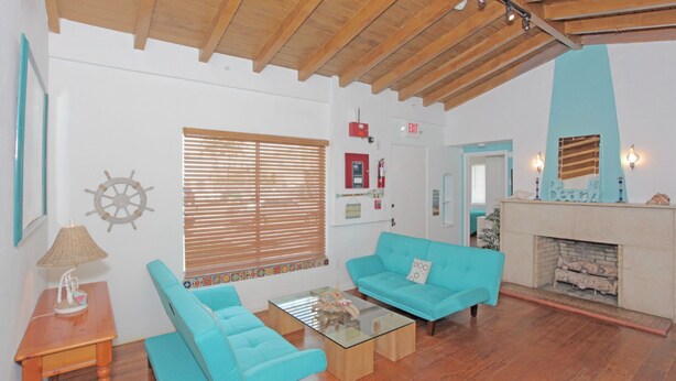 A living room with wooden flooring, a blue sofa, a glass coffee table, a wooden side table, and a fireplace. - The South Beach Party House (Miami Beach)