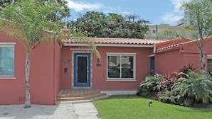 A single-story house with a red exterior, a front door, and a small front yard with plants and a bird. - The South Beach Party House (Miami Beach)