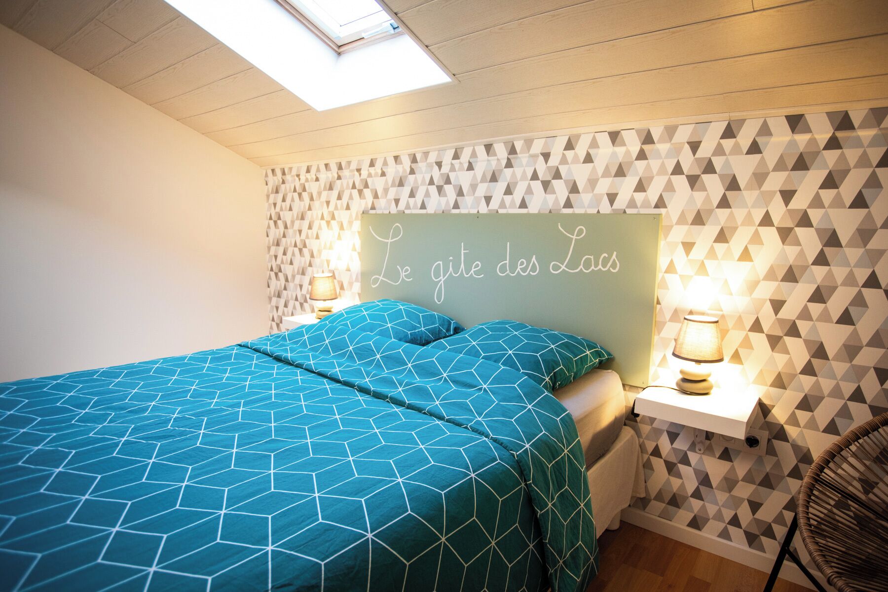 A bedroom with a geometric-patterned bedspread, a headboard with a French phrase, and a geometric-patterned wall.