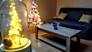 Un salon avec un sapin de Noël sous une cloche de verre, un sapin de Noël décoré et un canapé.
