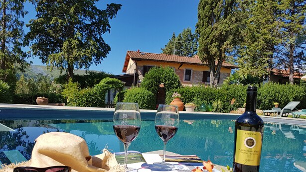Escena junto a la piscina con una botella de vino, dos copas de vino tinto, un sombrero de paja, gafas de sol y un menú.