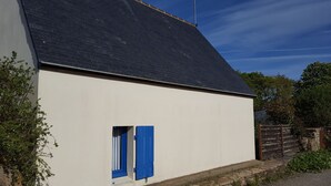 Ein eingeschossiges Gebäude mit dunklem Dach und einem kleinen Fenster mit blauen Fensterläden.