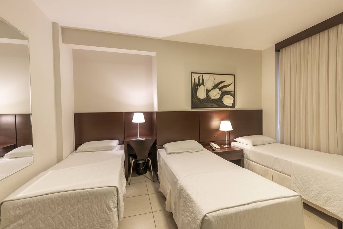 Habitación de hotel con dos camas individuales, un escritorio con silla, teléfono y un cuadro en la pared.