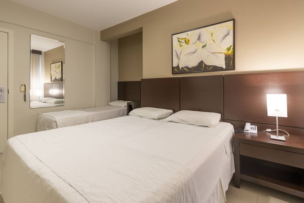 Una habitación de hotel con una cama grande, una mesita de noche con lámpara, un teléfono y un cuadro de flores en la pared.