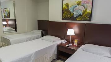 Habitación de hotel con dos camas individuales, una mesita de noche con lámpara, teléfono y un cuadro de flores en la pared.