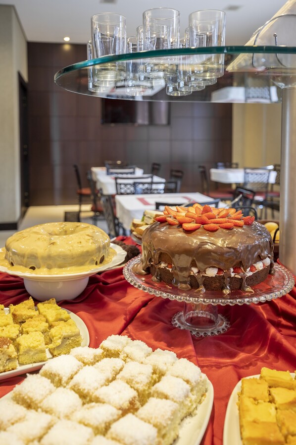 Una mesa de buffet con diversos postres, incluyendo un pastel de chocolate con fresas, un pastel amarillo y otras vienecitas.