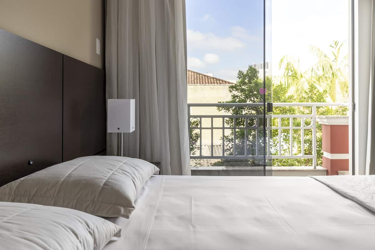 Una habitación de hotel con cama, mesita de noche, ventana con cortinas y vistas al exterior.