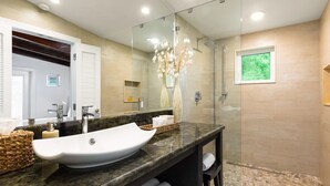 A modern bathroom with a large mirror, a white vessel sink, and a glass-enclosed shower.