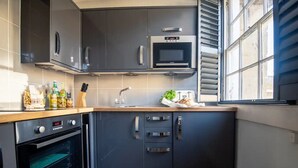 Una cocina moderna con armarios oscuros, microondas, horno y ventana con persianas.