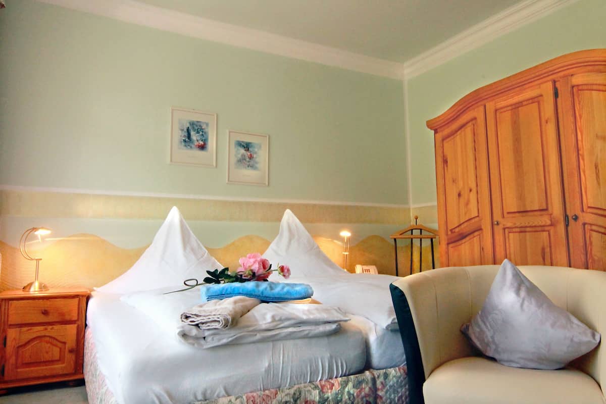 A neatly made bed with pillows, a bedside lamp, and a wooden cabinet in a room with light green walls.