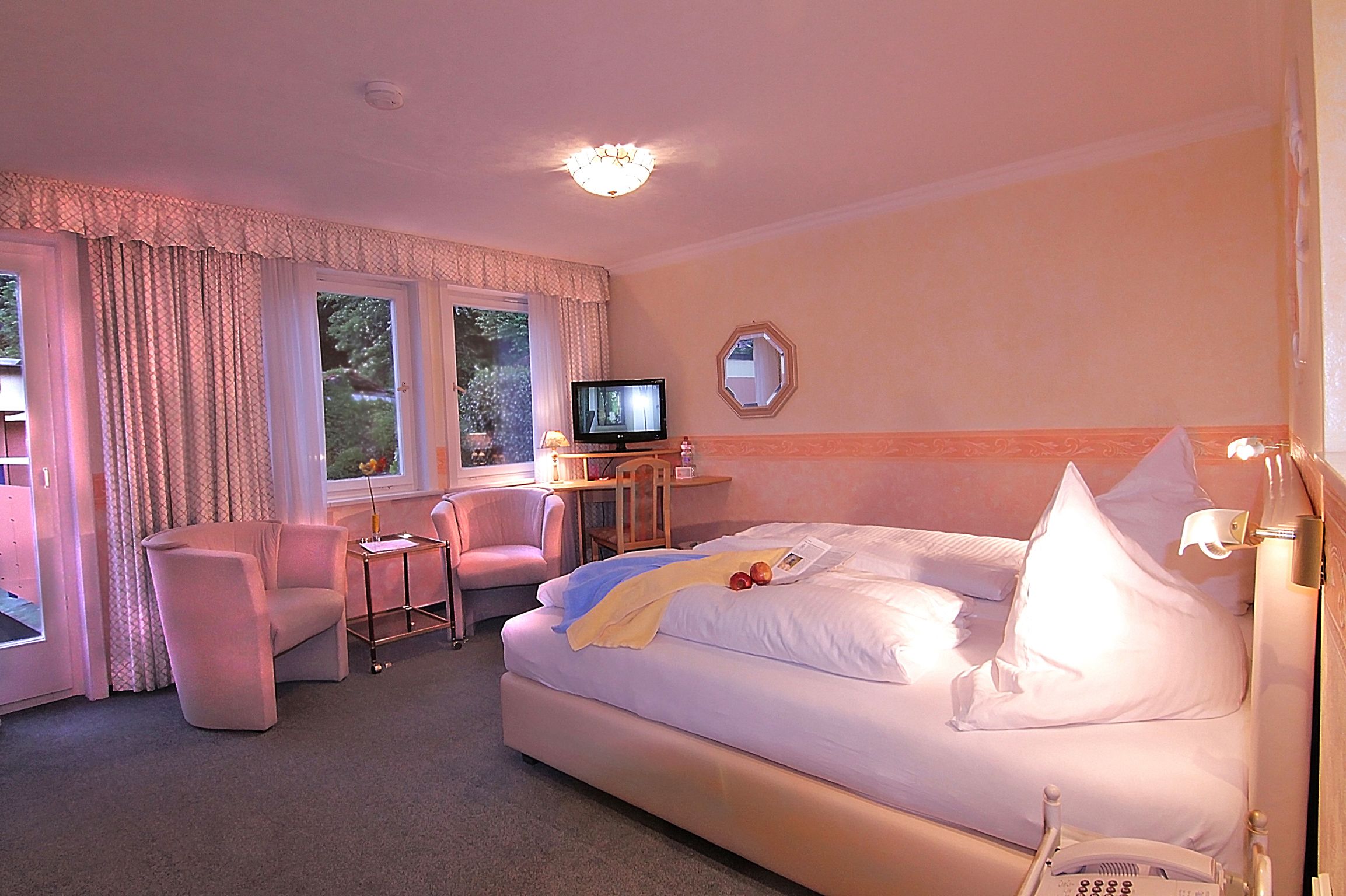 Una habitación de hotel con una cama, un escritorio con televisor, una silla y una ventana con cortinas.