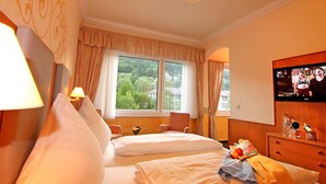 A hotel room with two beds, a television, and a window with a view of trees and buildings.