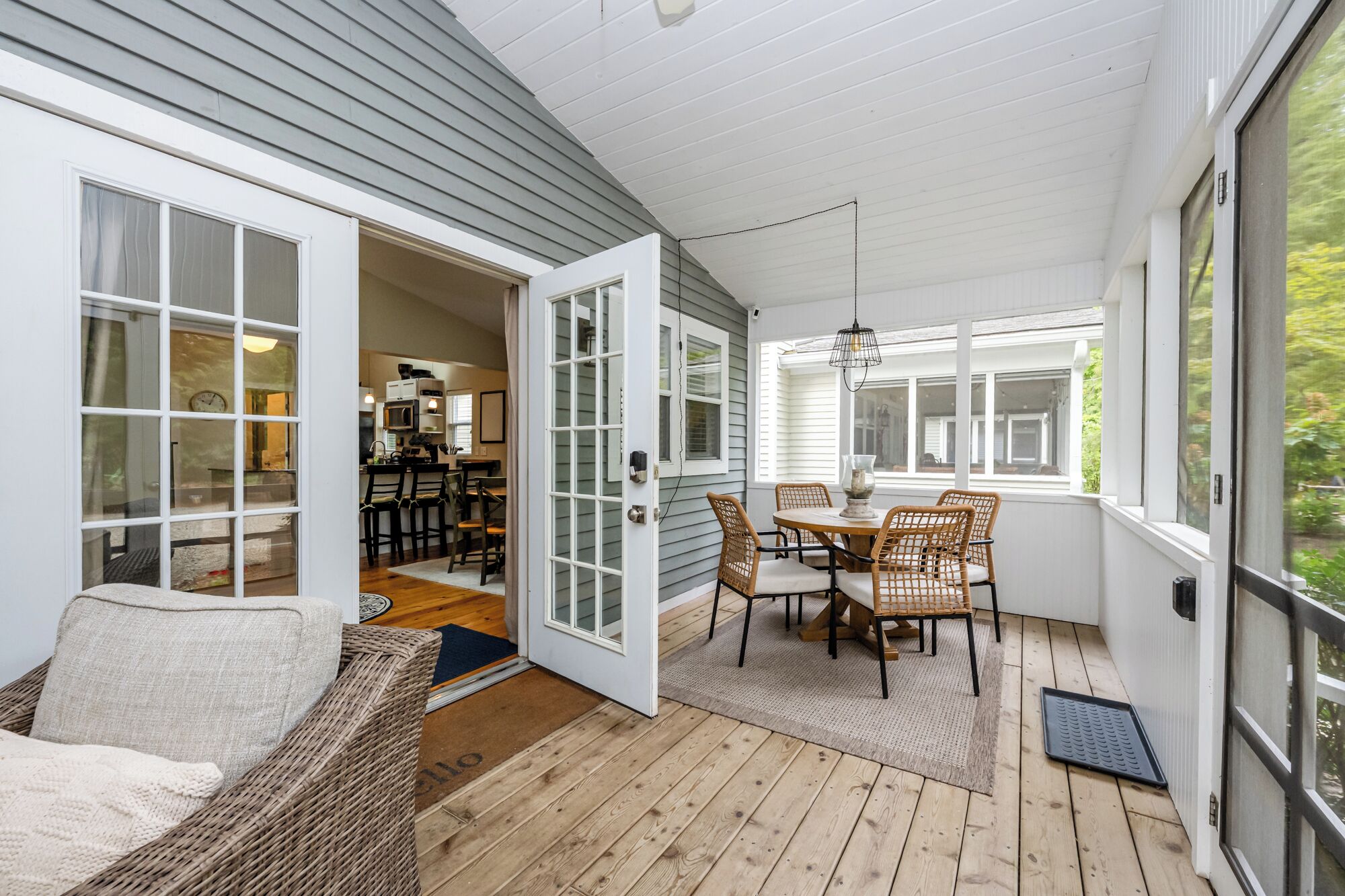 A covered patio with a dining table and chairs, a wicker sofa, and a view of the kitchen through an open door.