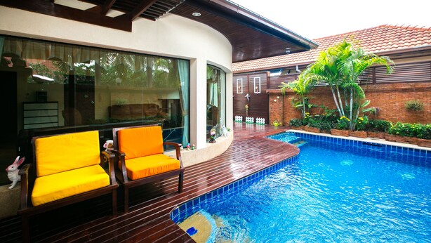 A swimming pool with a wooden deck and yellow chairs, surrounded by a brick wall and greenery.