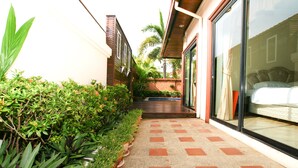A pathway leading to a bedroom with a glass door, surrounded by potted plants and a brick wall.