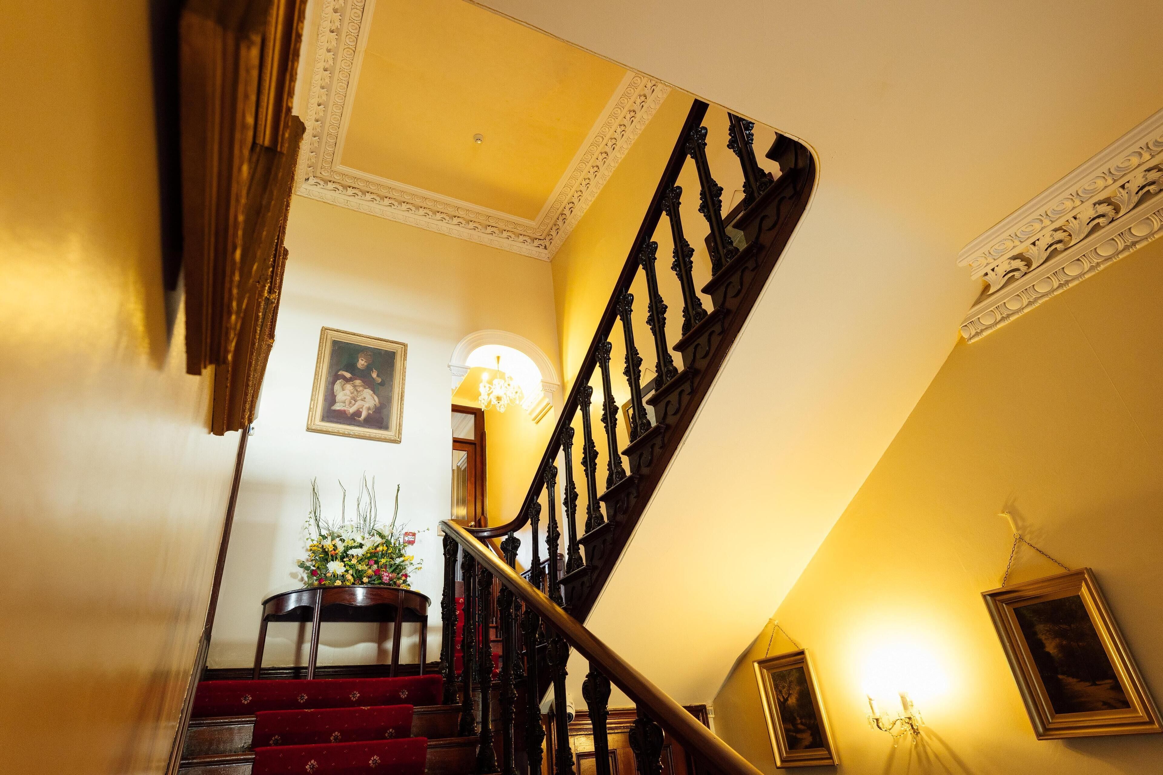 Un magnifique escalier avec des rampes richement décorées et un palier recouvert d’une moquette rouge.
