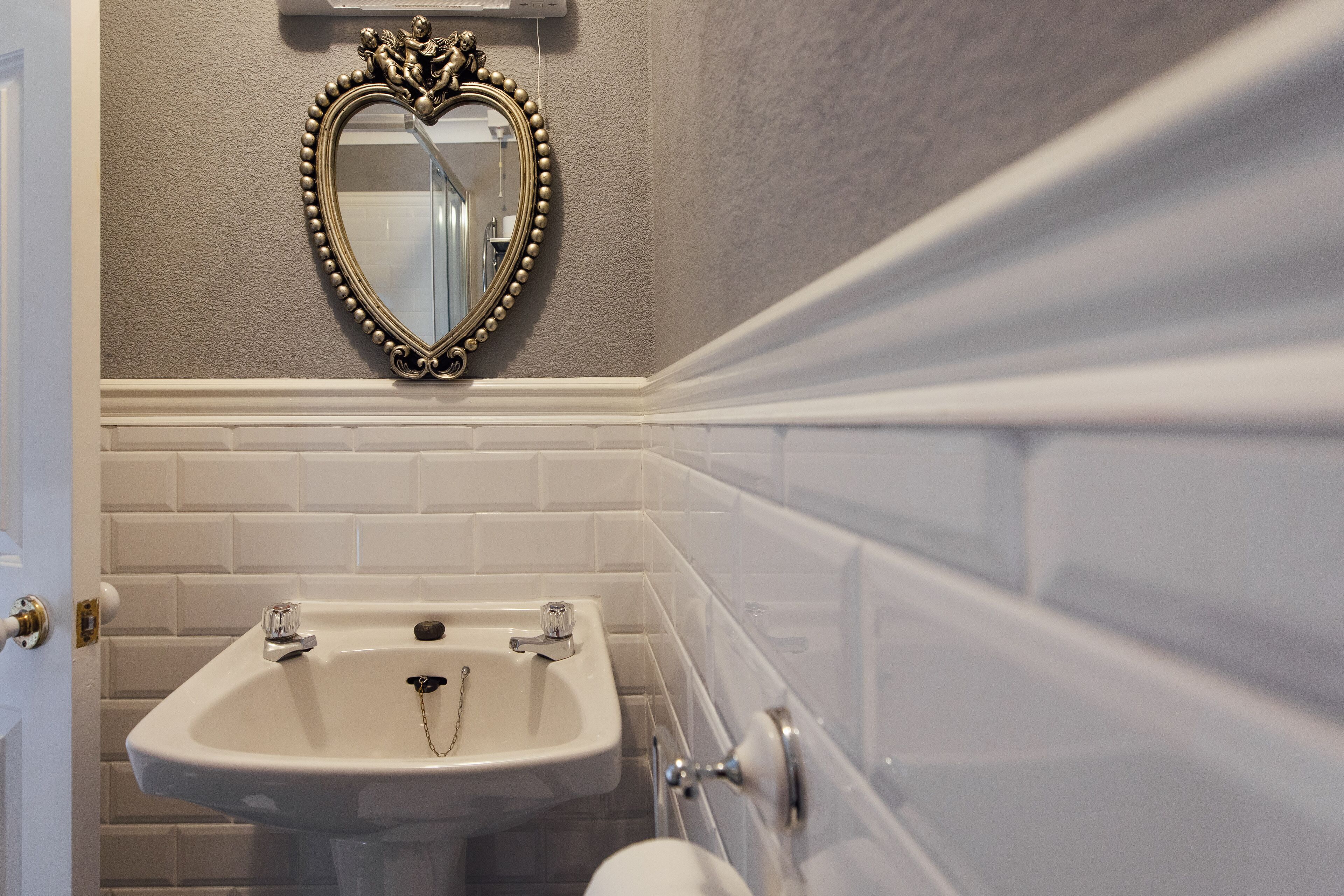 A bathroom with a white sink, a mirror with a decorative frame, and white tiled walls.