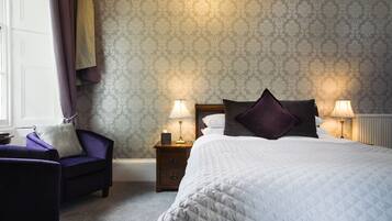 A bedroom with a bed, two bedside tables with lamps, a chair, and a window with curtains.