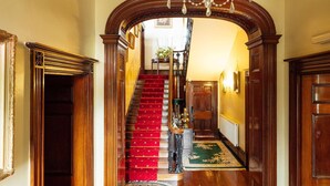 A grand hallway with a red carpet, ornate woodwork, and a chandelier. - Elm Grove Country House (Tenby)