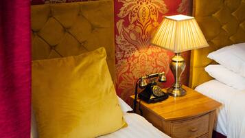 A hotel room with a tufted headboard, a wooden nightstand with a lamp and a rotary phone, a yellow pillow, and a white bed.