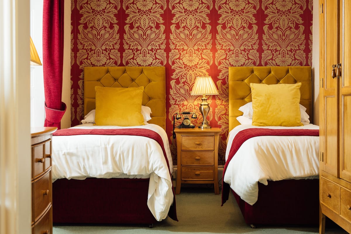 Une chambre d’hôtel avec deux lits, une table de chevet en bois, une lampe et une armoire.