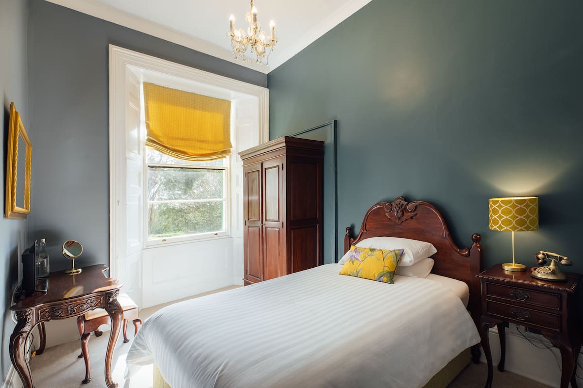 Une chambre avec un grand lit, une armoire en bois, une table de chevet avec une lampe et une fenêtre ornée de rideaux jaunes.